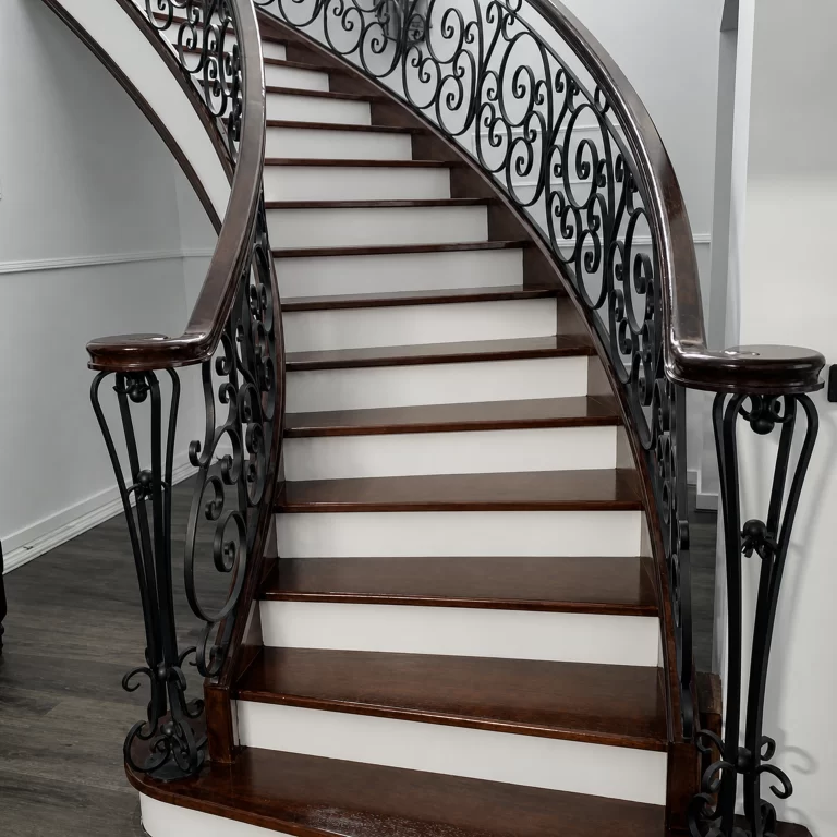 Curved timber staircase with ornate black lacework balustrade